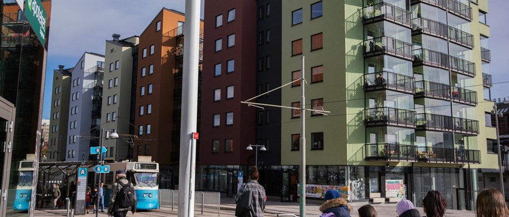 Vy från Gamlestans torg. Det är sommar och ett par spårvagnar är på väg in till hållplatsen och de väntande resenärerna.